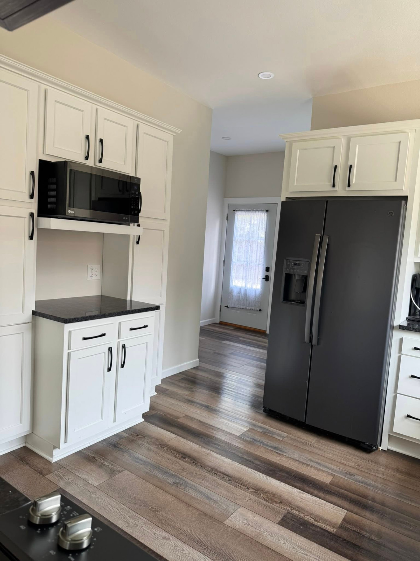 Bright kitchen with white cabinets, black appliances, and freshly cleaned wood-look floors