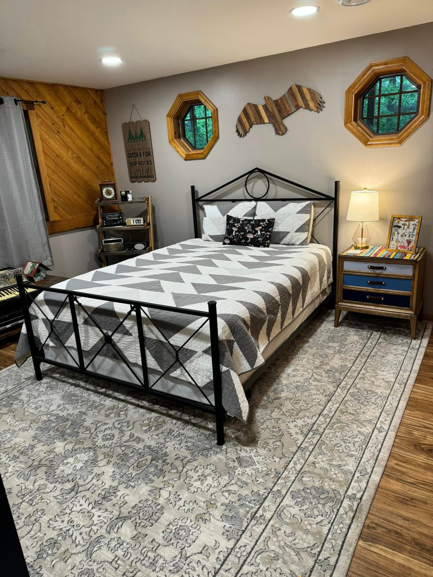 Guest bedroom with a black metal bed, gray patchwork quilt, and rustic wood accents