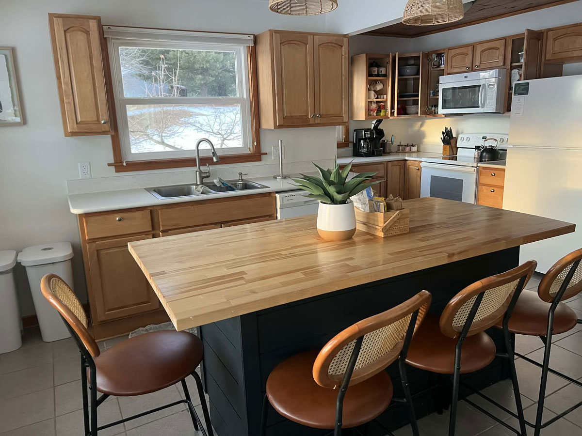 Clean wood kitchen with a large island, four stools, and a potted plant centerpiece