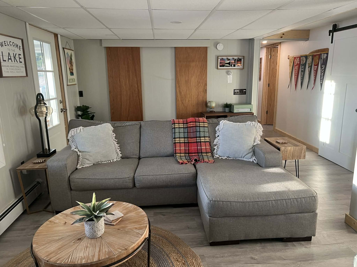 Tidy lake house living room with a gray sectional, plaid throw, and wood coffee table