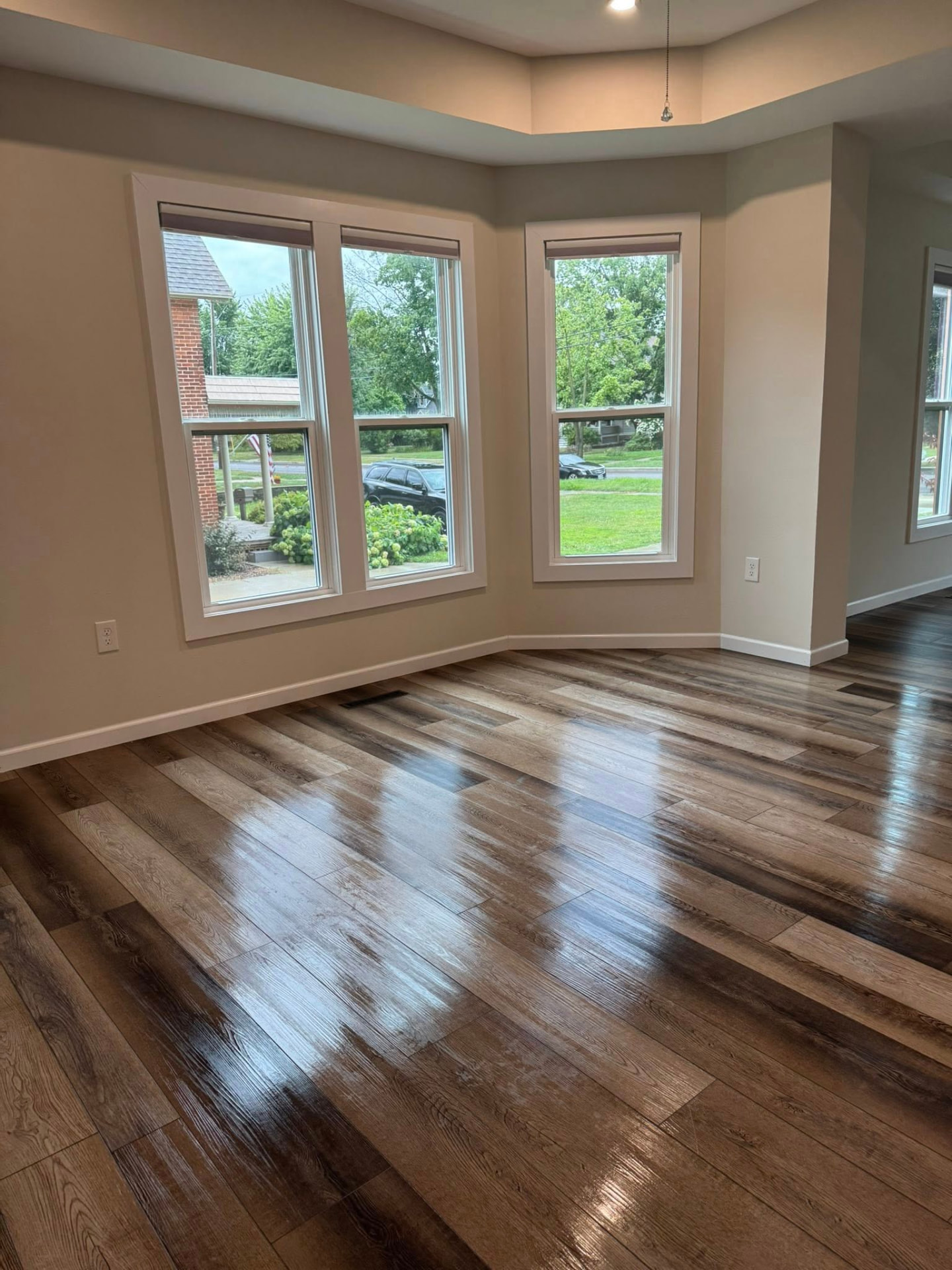 Empty sunlit room with clean wood-look floors and three tall windows