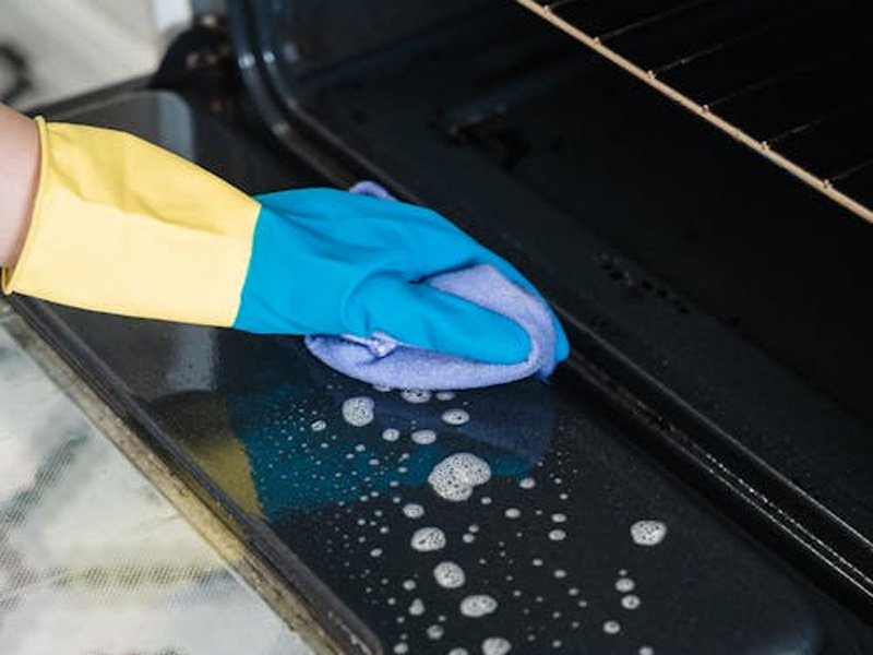 Gloved hand deep-cleaning the inside of an oven